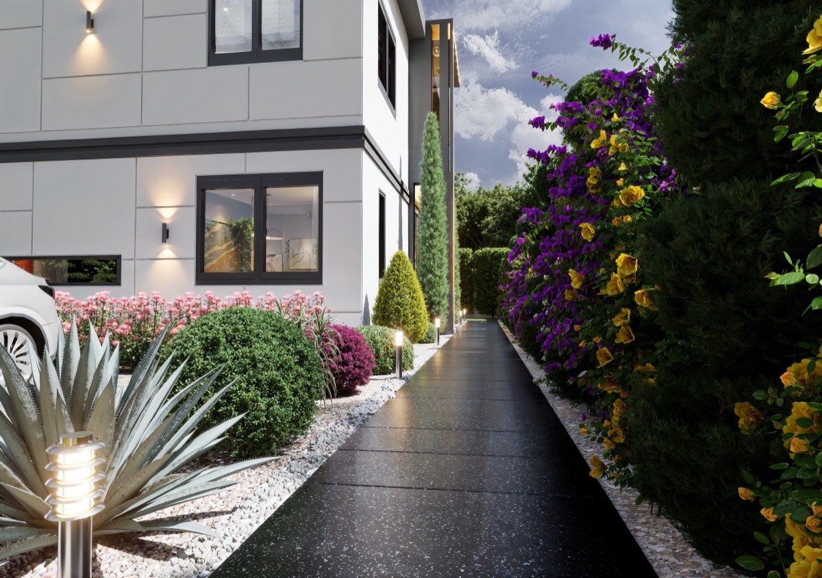 Side approach at dusk: stone paving, planted borders and facade lighting